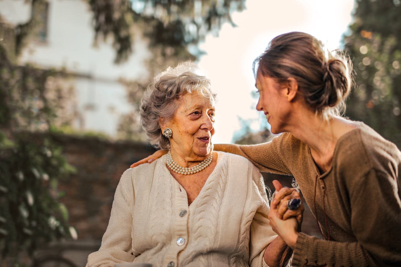 gallery-3 Elderly woman and adult daughter share a joyful, affectionate moment in a sunny garden.