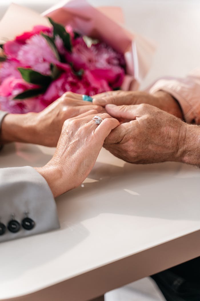about-01 Tender moment of elderly and young hands holding with pink flowers, symbolizing care and love.